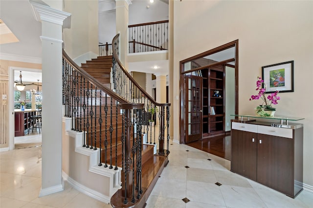 interior space featuring tile patterned flooring, crown molding, a towering ceiling, and decorative columns