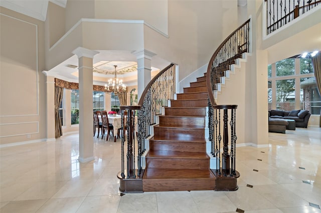 stairway featuring a notable chandelier, decorative columns, plenty of natural light, and a towering ceiling