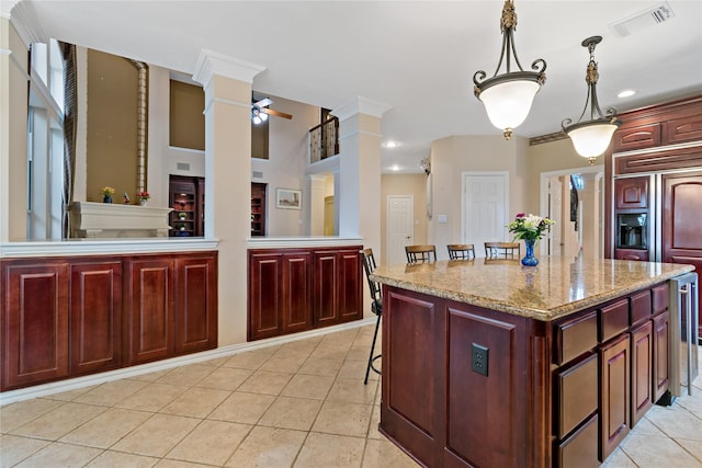 kitchen featuring visible vents, dark brown cabinets, a center island, light tile patterned floors, and ornate columns