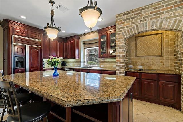 kitchen with paneled fridge, visible vents, reddish brown cabinets, backsplash, and a center island