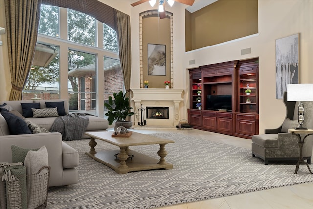 tiled living room featuring visible vents, a high ceiling, a warm lit fireplace, and ceiling fan