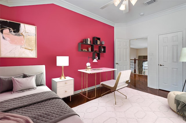 bedroom featuring wood finished floors, visible vents, baseboards, an accent wall, and crown molding