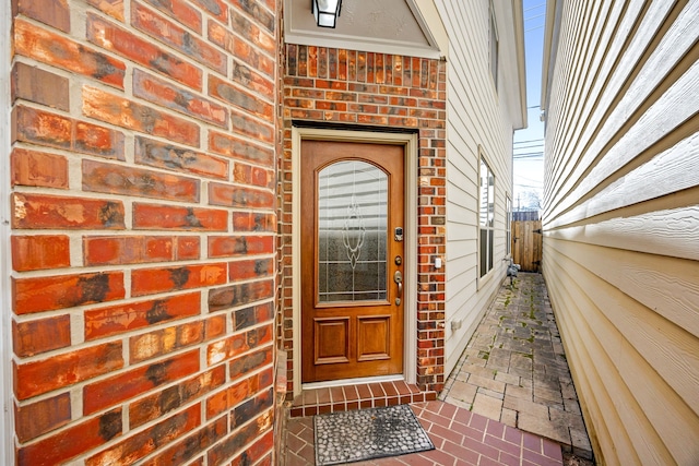 view of exterior entry featuring fence and brick siding