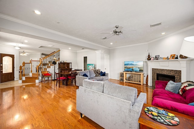 living area featuring visible vents, a glass covered fireplace, stairway, light wood finished floors, and ceiling fan