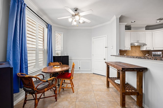 dining space with ceiling fan, crown molding, light tile patterned floors, and wainscoting