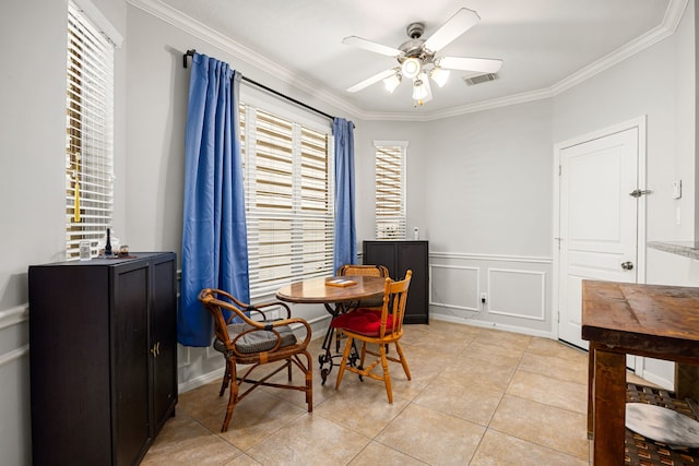 dining room featuring light tile patterned floors, a ceiling fan, visible vents, crown molding, and a decorative wall