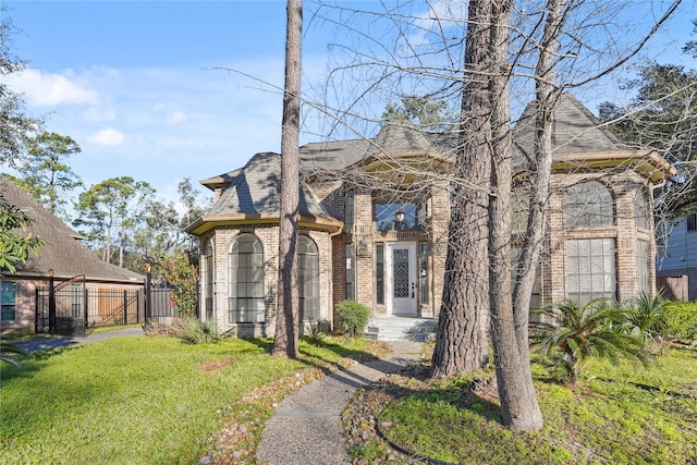 view of front of property with brick siding, a shingled roof, a front yard, and fence