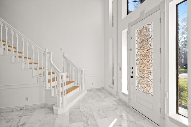 foyer entrance featuring plenty of natural light, marble finish floor, stairs, and a towering ceiling