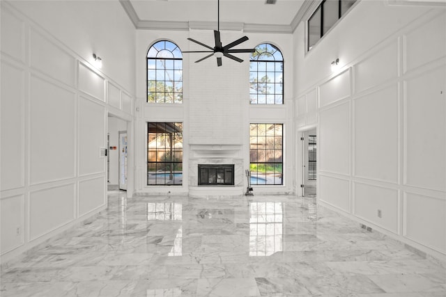 unfurnished living room featuring a decorative wall, marble finish floor, crown molding, and a healthy amount of sunlight