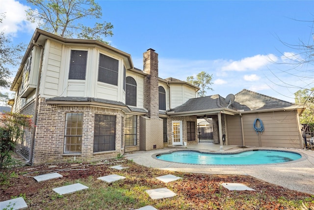 back of house featuring an outdoor pool, a patio area, brick siding, and a chimney