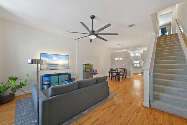 living room with visible vents, light wood finished floors, baseboards, stairs, and ceiling fan with notable chandelier