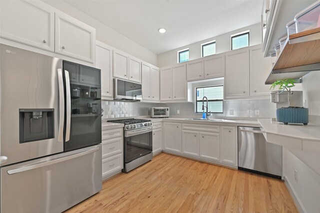 kitchen with backsplash, light countertops, light wood-style floors, stainless steel appliances, and a sink