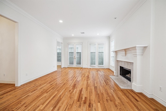 unfurnished living room with a tiled fireplace, light wood-style flooring, french doors, and ornamental molding