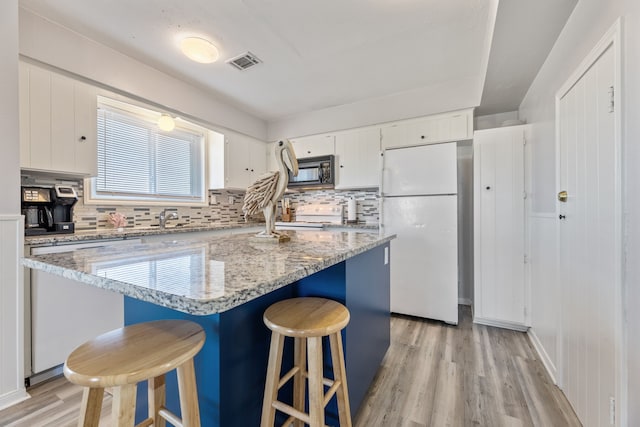 kitchen with visible vents, black microwave, a breakfast bar, light wood-style flooring, and freestanding refrigerator