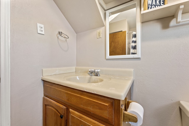 full bath with vanity, lofted ceiling, and a textured wall