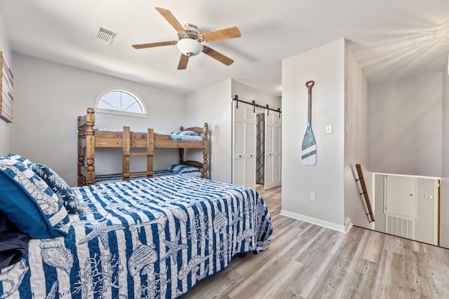 bedroom with visible vents, ceiling fan, baseboards, a barn door, and wood finished floors