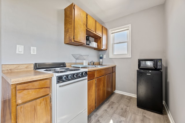 kitchen with a sink, light countertops, light wood-style flooring, and white range with electric stovetop