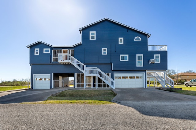 raised beach house featuring stairs, an attached garage, and asphalt driveway
