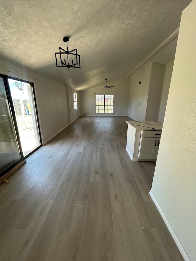 interior space featuring lofted ceiling, wood finished floors, baseboards, and a textured ceiling