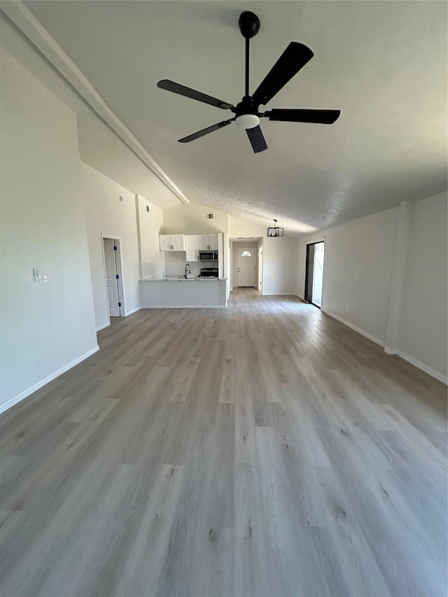 unfurnished living room with a sink, light wood finished floors, baseboards, ceiling fan, and vaulted ceiling