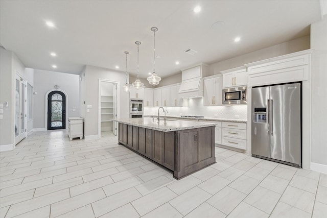 kitchen with tasteful backsplash, light stone countertops, appliances with stainless steel finishes, custom exhaust hood, and white cabinets