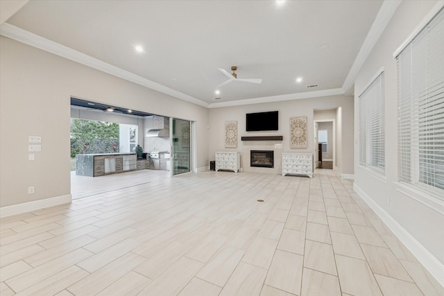 unfurnished living room with a glass covered fireplace, crown molding, and ceiling fan