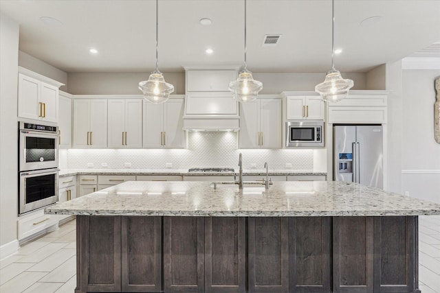 kitchen featuring visible vents, a center island with sink, appliances with stainless steel finishes, white cabinetry, and a sink