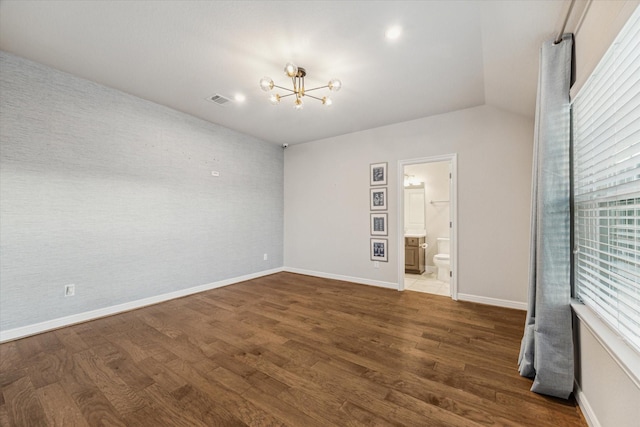 spare room featuring visible vents, dark wood-type flooring, baseboards, a chandelier, and vaulted ceiling