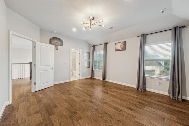 unfurnished room with visible vents, wood finished floors, baseboards, lofted ceiling, and a chandelier