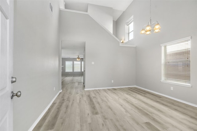 interior space featuring visible vents, ceiling fan with notable chandelier, a high ceiling, light wood finished floors, and baseboards