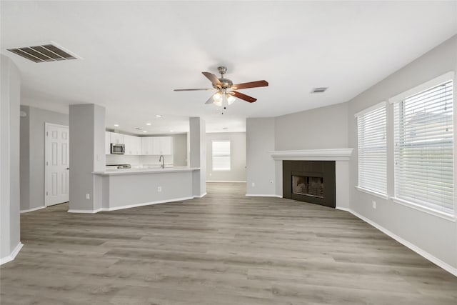 unfurnished living room with visible vents, ceiling fan, a fireplace, and light wood-style flooring