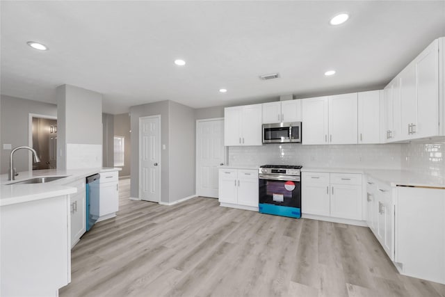 kitchen with backsplash, appliances with stainless steel finishes, light wood-style floors, and a sink