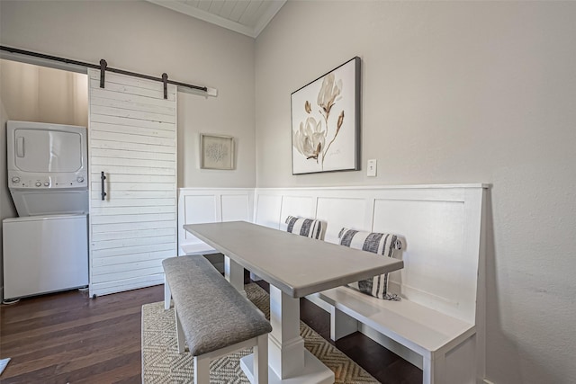 dining area with a barn door, crown molding, stacked washer / drying machine, and dark wood-style flooring