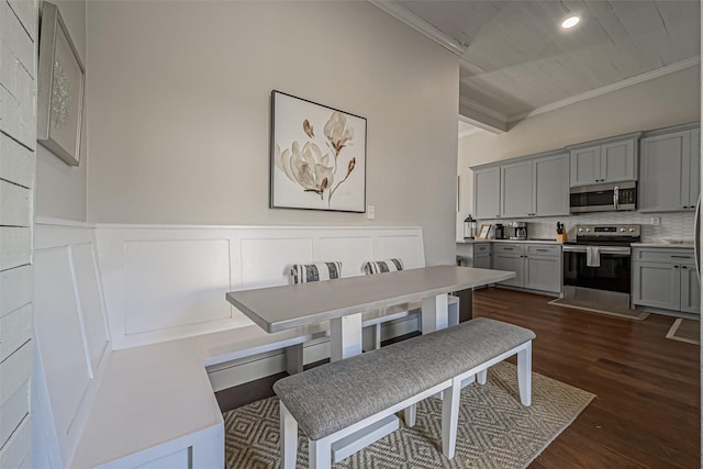 dining area featuring beamed ceiling, dark wood-type flooring, ornamental molding, wainscoting, and a decorative wall