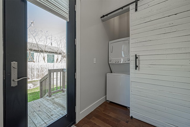 clothes washing area featuring stacked washer / dryer, baseboards, a barn door, and dark wood-style flooring