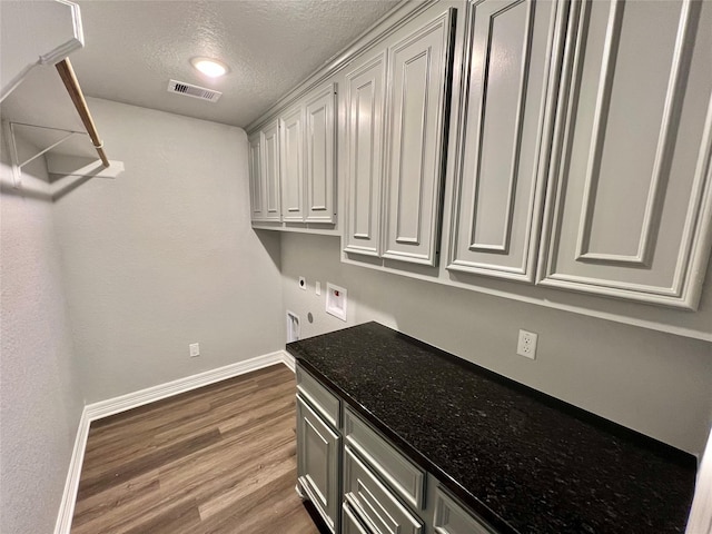 laundry room with visible vents, a textured ceiling, wood finished floors, cabinet space, and baseboards