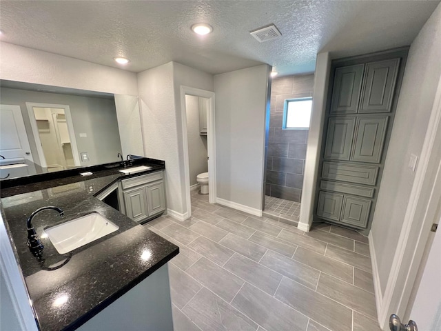 bathroom with visible vents, double vanity, a sink, a walk in shower, and toilet