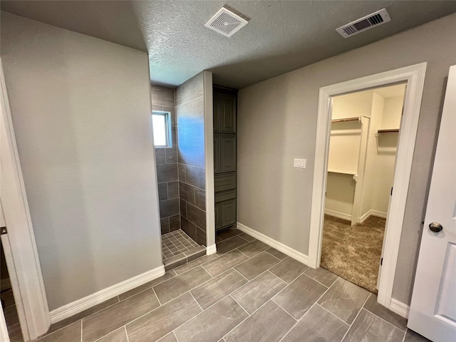 bathroom with visible vents, baseboards, a textured ceiling, and a walk in shower