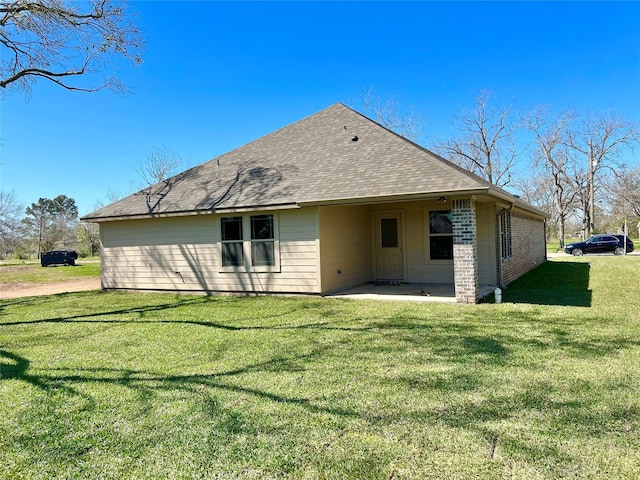 rear view of property featuring brick siding, a patio, a shingled roof, and a yard