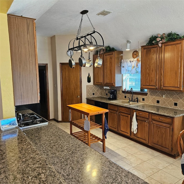 kitchen with dark countertops, visible vents, decorative backsplash, brown cabinets, and a sink