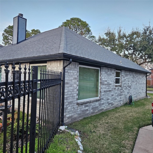 view of home's exterior with a lawn, fence, a shingled roof, brick siding, and a chimney