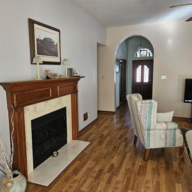 living room featuring baseboards, arched walkways, a high end fireplace, dark wood-type flooring, and a textured ceiling