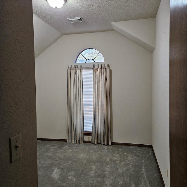 carpeted empty room featuring visible vents, lofted ceiling, a textured ceiling, and baseboards