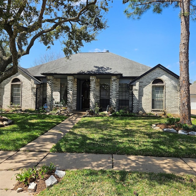 view of front of house with a front yard, brick siding, and roof with shingles