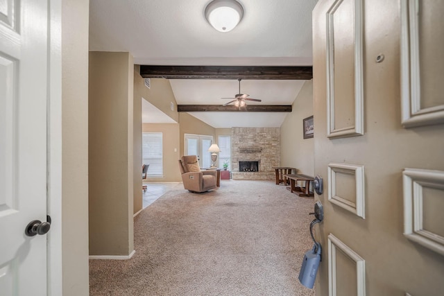 carpeted living room with a stone fireplace, lofted ceiling with beams, baseboards, and ceiling fan