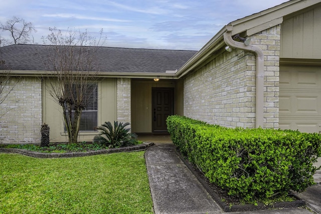 property entrance featuring an attached garage, a lawn, brick siding, and a shingled roof