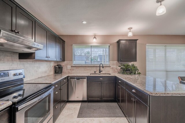 kitchen featuring tasteful backsplash, under cabinet range hood, a peninsula, stainless steel appliances, and a sink