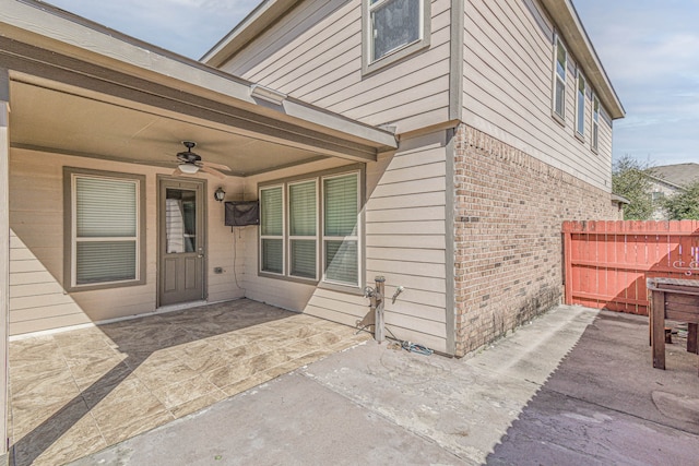 property entrance with brick siding, a patio area, a ceiling fan, and fence