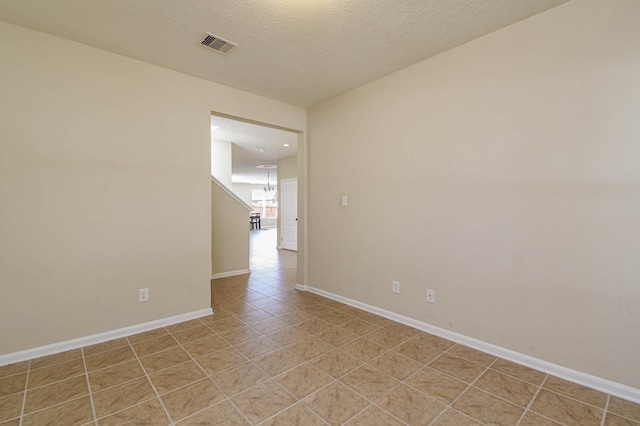 empty room featuring light tile patterned floors, visible vents, baseboards, and a textured ceiling