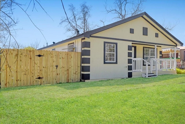 back of property with a porch, fence, a lawn, and stucco siding